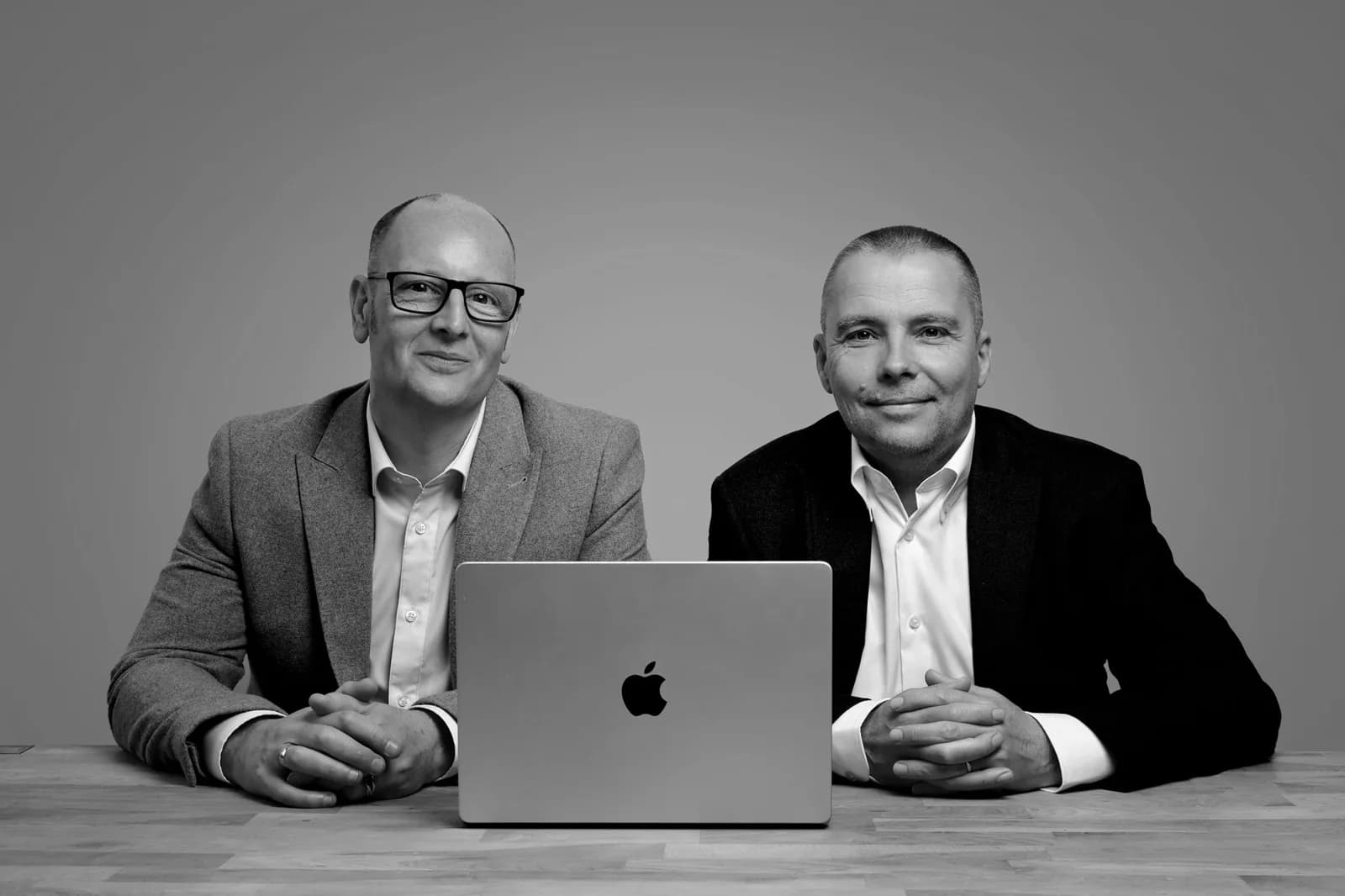 David Todd and Jay Rendell sitting side by side at a desk with a laptop, in black and white.